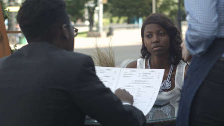Afro american man ordering in outside cafe, while sitting with his female partnerの写真素材