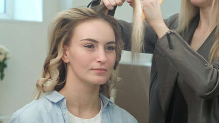 Professional hair stylist doing hairstyle of beautiful blond model and she smilingの写真素材