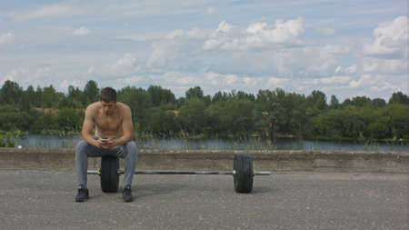 Male sportsman using his mobile phone while taking break after active intense training outdoorsの写真素材