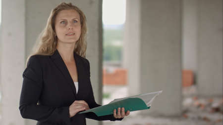 Female architect studying drafts while visiting large construction siteの写真素材