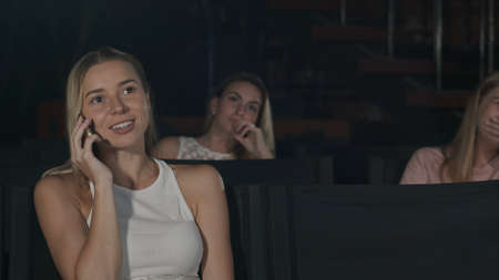 Young woman on the phone during movie at the cinemaの写真素材