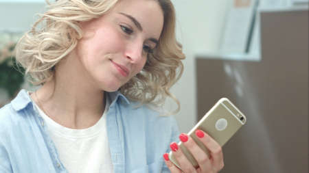 Pensive young woman use cell phone at salon in the morningの写真素材