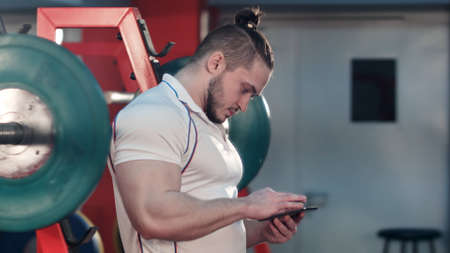 Muscular man using phone in the gym between exercisesの写真素材