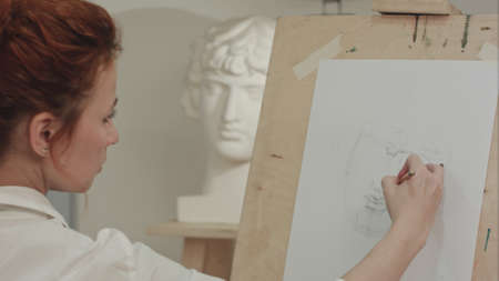 Concentrated woman artist painting plaster bust in art studioの写真素材