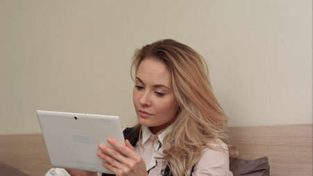 Smiling nice young woman uses a digital tablet doing on-line shopping sitting on a bed at homeの写真素材