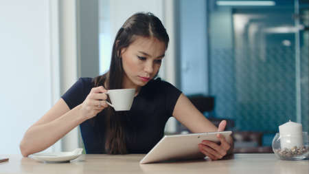 Young woman using digital tablet while drinking coffee or tea at a cafeの写真素材