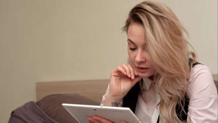 Excited smiling woman having video call on tablet while sitting on her bedの写真素材