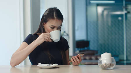 Beautiful girl drinking coffee and using phone in a cafeの写真素材