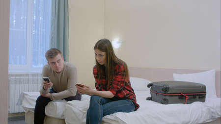 Couple sitting on the bed, not talking to each other after quarrel, typing on smartphonesの写真素材