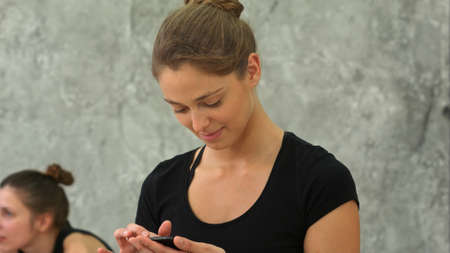 Attractive happy young woman doing yoga and using cell phone sitting on the floorの写真素材