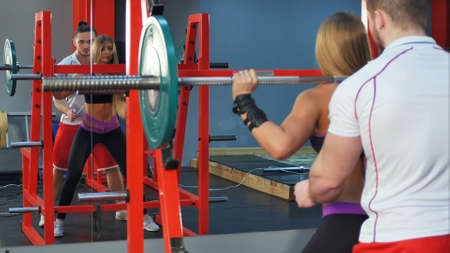 Personal trainer helping female client lifting barbell at the gymの写真素材