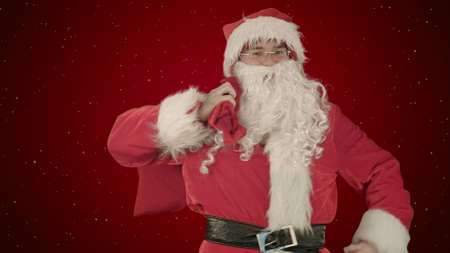 Real Santa Claus carrying presents in his sack on red background with snowの写真素材