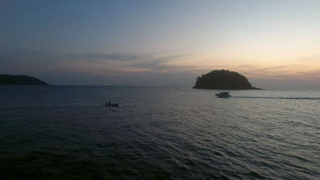 Aerial drone footage of flight above calm water, near wild island and yacht driving in sunset soft lighの写真素材