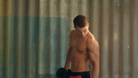 Torso shot of a young man with bare chest lifting dumbbellsの写真素材