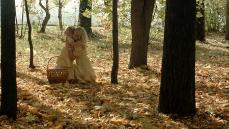 Happy mother with yellow maple leaflets hugs her daughter in autumn forestの写真素材