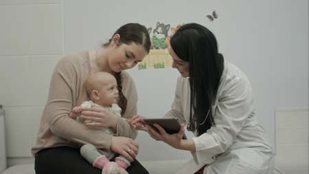 female doctor play with newborn baby and shows tablet  to motherの写真素材