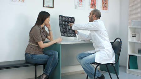 Male doctor showing xray results to worried female patient and filling in formの写真素材