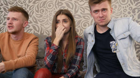 Teen friends watching scary movie in television and shutting eyes and coverng facesの写真素材