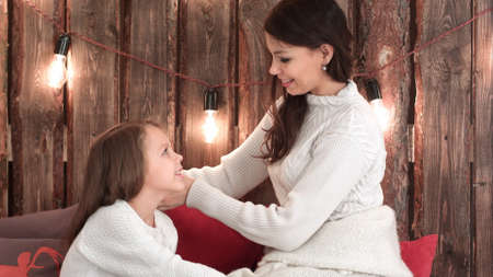 Young mother in white sweater plaiting her daughter hairの写真素材