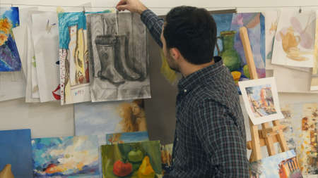 Young man hanging paintings on string in art classの写真素材