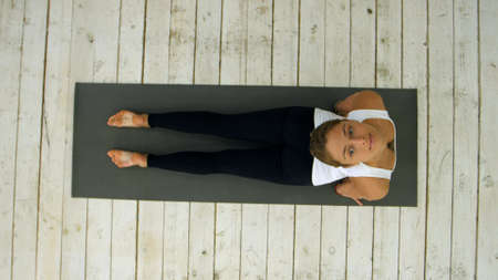 Beautiful young woman working out indoors, doing yoga exercise in the room, downward facing dog pose, adho mukha svanasana sun salutation poseの写真素材