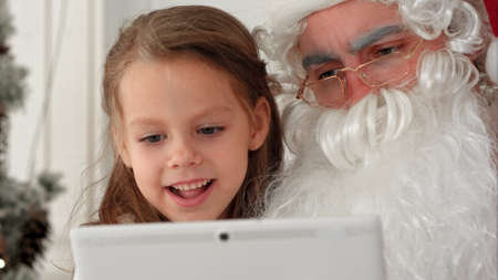 Little smiling girl sitting with Santa using tabletの写真素材