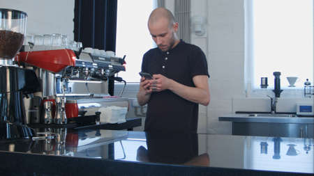Male barista using smartphone at work placeの写真素材