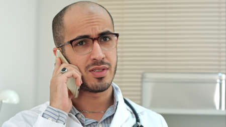 Young male doctor in glasses talking on mobile phoneの写真素材