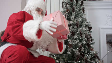 Santa Claus opening his sack and putting presents under the Christmas treeの写真素材