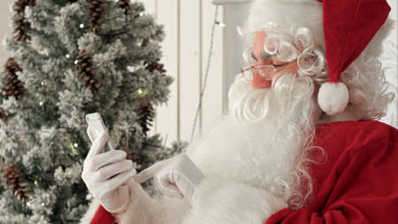Happy Santa Claus checking up Christmas emails from kids on his phoneの写真素材