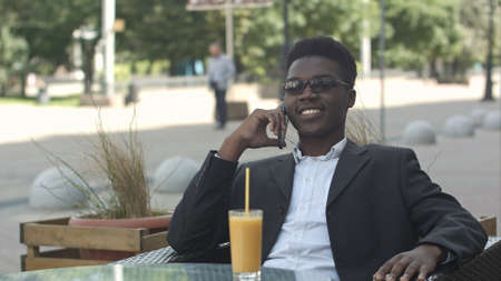 Positive afro american marketing expert in eyewear and casual outfit having phone call in cafeの写真素材