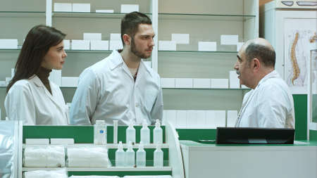 Elderly pharmacist and assistants talking seriously at farmacy receptionの写真素材