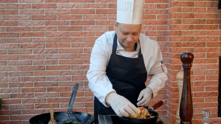 Handsome male chef dressed in white uniform decorating paella and looking at the camera smilingの写真素材