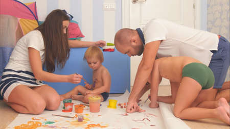 Happy mother, father and their little sons painting with watercolors in the nursery roomの写真素材