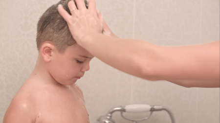 Mother washing her little boy in bath while he is blowing bubblesの写真素材