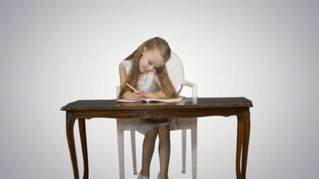 Cute little girl doing homework, writing down on white backgroundの写真素材