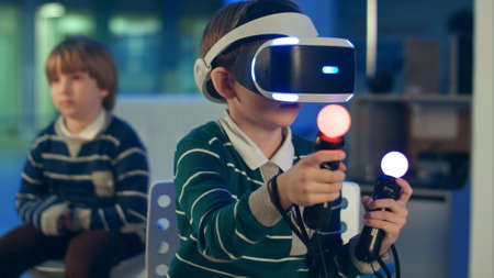 Little boy in vr headset playing virtual reality game with controllers while another boy waiting for his turnの写真素材