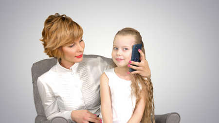 Little daughter having phone call, sitting near her mother on white backgroundの写真素材