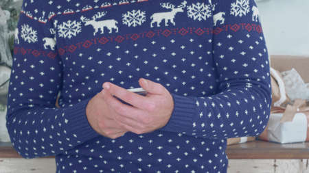 Young man in Christmas knitwear holding phone in his handsの写真素材