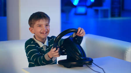 Happy excited little boy playing videogame with racing wheelの写真素材