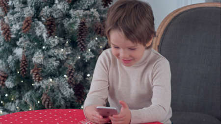 Little happy boy using smart phone at home decorated for Christmasの写真素材