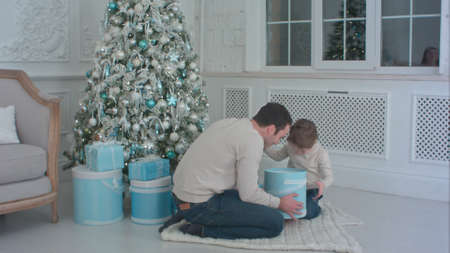 Smiling father and his happy son opening presents sitting next to the Christmas treeの写真素材