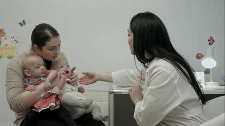 Female pediatrician doctor explain something to mother with newborn baby twins at modern hospital indoorsの写真素材