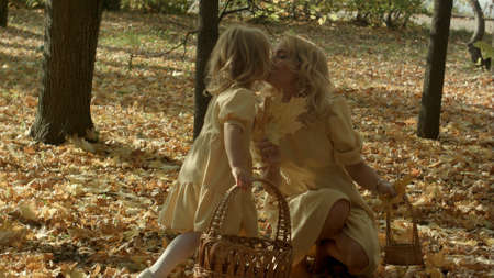 Mother and daughter play in autumn park. Parent and child walk in the forest on a sunny fall day. Children playing outdoors with yellow maple leaf.の写真素材
