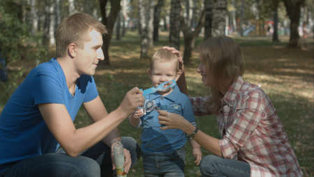 Boy is playing together with his parents. They are playing with soap-bubbles.の写真素材