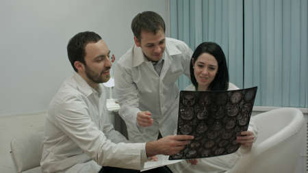 Two physicians in good mood analyze results of patient to diagnose disease, then comes intern with...
