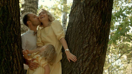 Happy couple with her little daughter kissing over a forest backgroundの写真素材