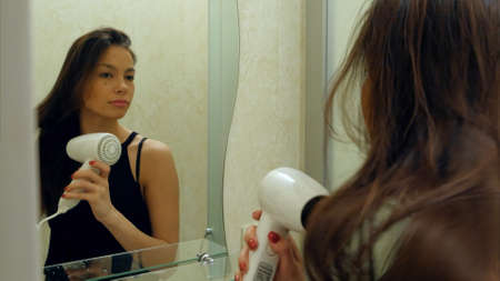 Young attractive girl dries hair with a hairdryer in a hotel bathroomの写真素材