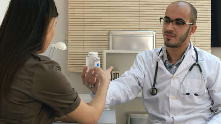 Male medical worker describing and giving pills to worried woman patientの写真素材