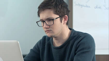 Young pensive student working on laptop at home office or library with serious faceの写真素材